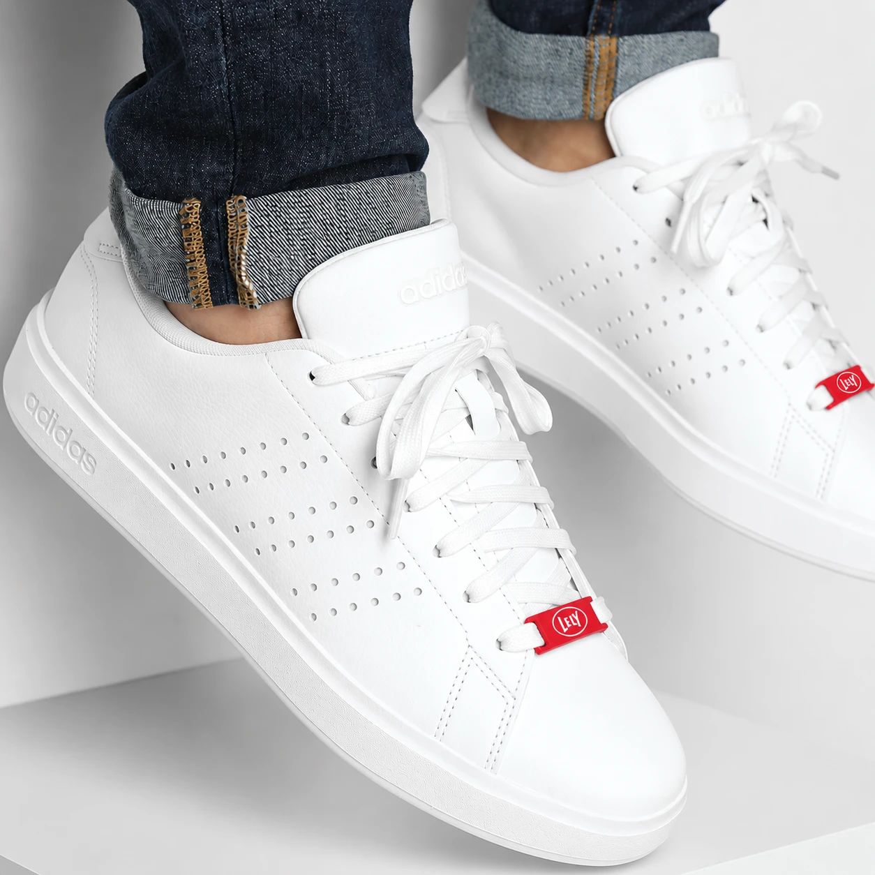 Weiße adidas Sneaker zur Jeans getragen, roter LaceTag mit Lely-Logo an den weißen Schnürsenkeln